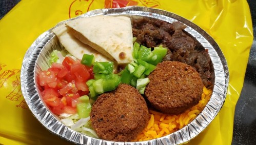 A foil container filled with rice, falafel, salad, and pita bread, set against a bright yellow background.
