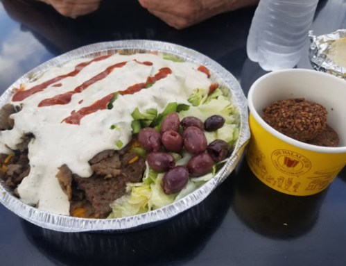 A foil bowl filled with salad, meat, and sauce, alongside a cup of brown dessert balls and a water bottle.