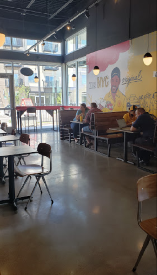 Interior of a casual restaurant with large windows, colorful wall art, and customers seated at tables.