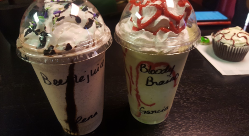 Two milkshake cups with whipped cream and colorful toppings, labeled "Beetlejuice" and "Bloody Brain."