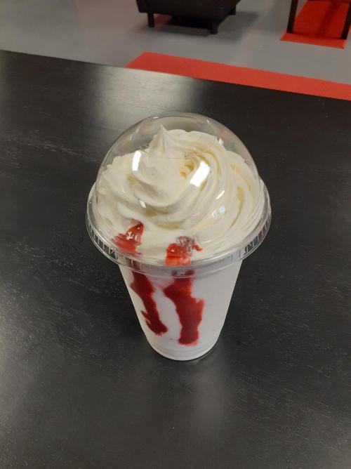 A clear cup filled with a creamy dessert topped with whipped cream and drizzled with red syrup.