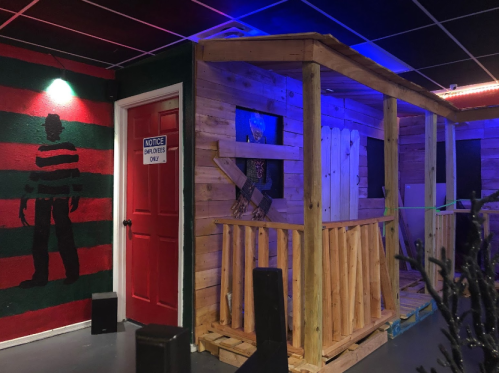 A wooden cabin structure with a red door, surrounded by colorful wall art and dim lighting.