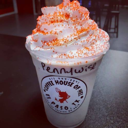 A frosty drink topped with whipped cream and orange sprinkles, labeled "Pennywise," in a coffee shop cup.