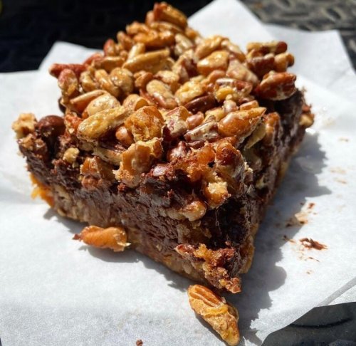 A close-up of a chocolate dessert topped with nuts, resting on a piece of parchment paper.