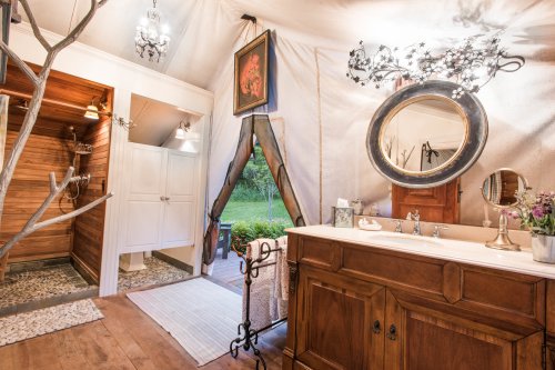 A stylish bathroom featuring a wooden vanity, round mirror, and a shower area with natural decor and elegant lighting.