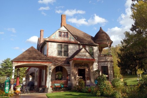A charming Victorian-style house with a turret, surrounded by greenery and under a blue sky with scattered clouds.