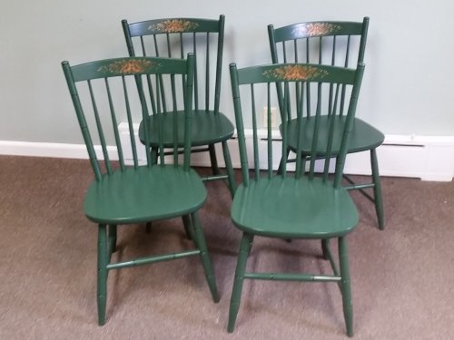 Four green wooden chairs with floral designs, arranged in a corner on a carpeted floor.