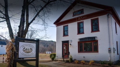 Historic white building with red trim, featuring a sign for The Hitchcock Chair Co. Ltd. and a tree in front.