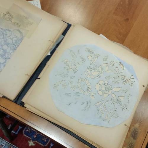 An open book displaying delicate floral patterns on translucent paper, resting on a wooden table.