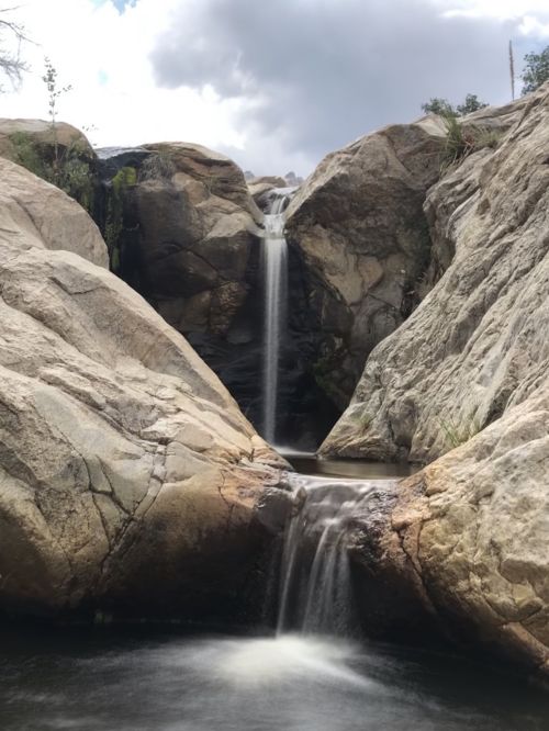 A serene waterfall cascading between large rocky formations under a cloudy sky.