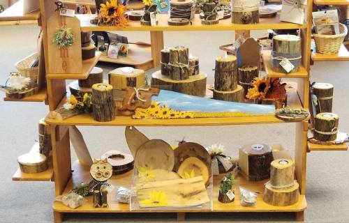 A display of rustic wooden crafts and decorations, featuring logs, flowers, and various handmade items on shelves.