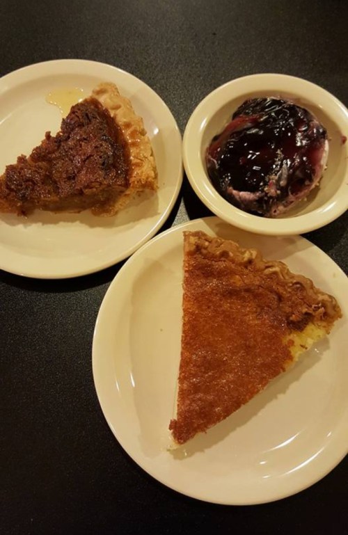 Two plates with slices of pie: one chocolate and one pecan, alongside a bowl of berry ice cream.
