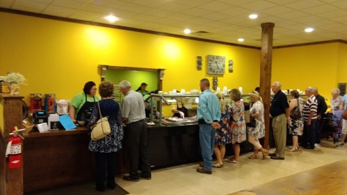 A line of people waiting at a buffet in a brightly colored restaurant with a friendly staff serving food.