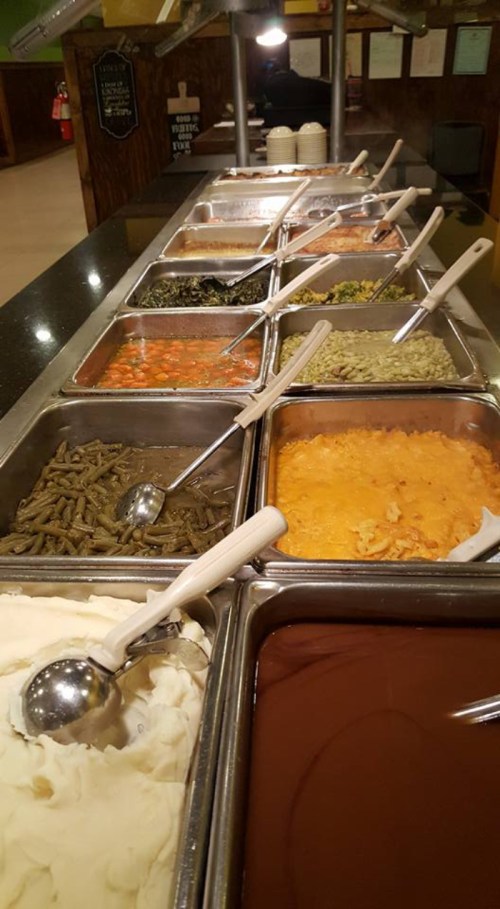 A buffet spread featuring various dishes in metal trays, including vegetables, casseroles, and sauces.