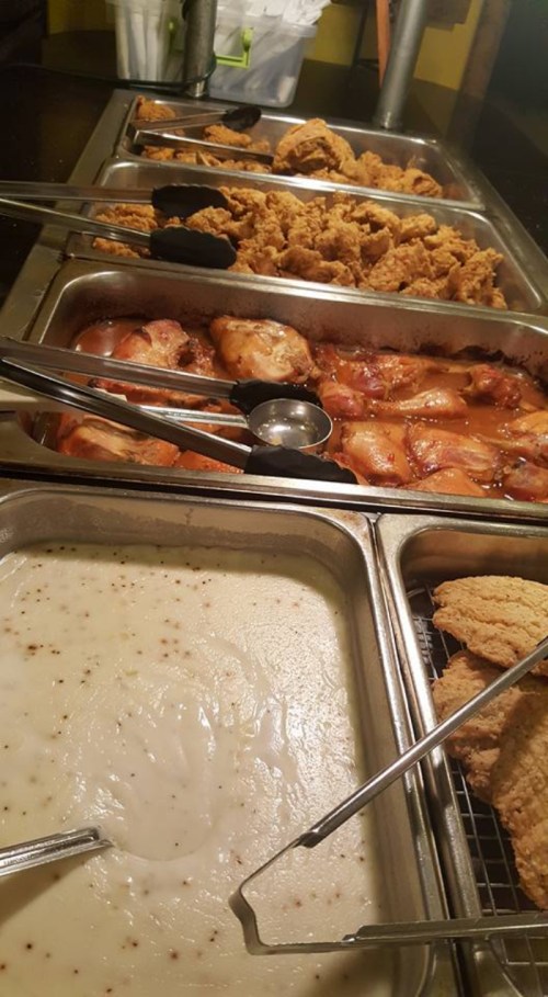 A buffet spread featuring fried chicken, various meats, and a serving of creamy gravy in metal trays.