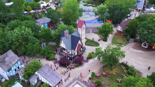 Aerial view of a vibrant park with a medieval-style building, surrounded by greenery and pathways filled with visitors.