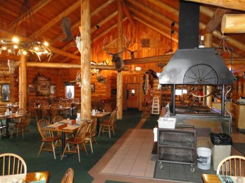 Cozy log cabin restaurant interior with wooden furniture, a large grill, and rustic decor featuring animal mounts.