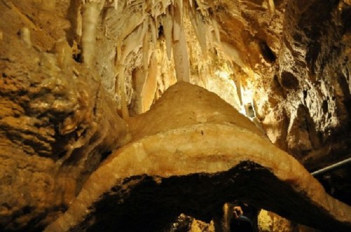 A view of a cave interior featuring stalactites and a large, curved rock formation illuminated by soft lighting.