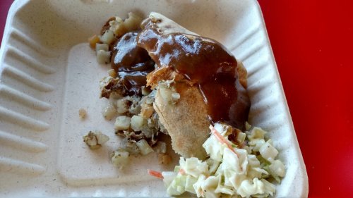 A partially eaten plate with a stuffed pastry, gravy, potatoes, and a side of coleslaw on a disposable tray.