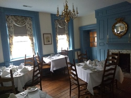 Cozy dining room with blue walls, wooden floors, and tables set with white tablecloths and glassware.