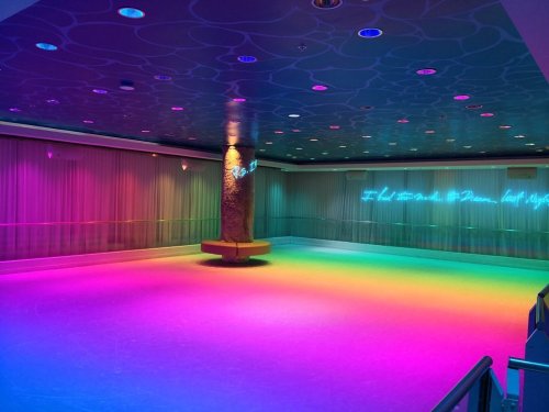 A brightly lit room with colorful neon lights and a smooth floor, featuring a central column and soft seating.