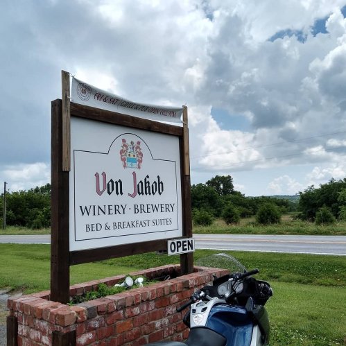 Sign for Von Jakob Winery, Brewery, and Bed & Breakfast Suites, with a motorcycle parked nearby and a cloudy sky.