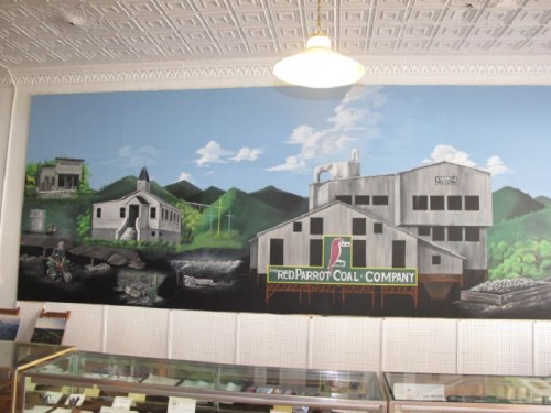 Mural of the Red Parrot Coal Company, featuring buildings and mountains, displayed on a wall in a shop.