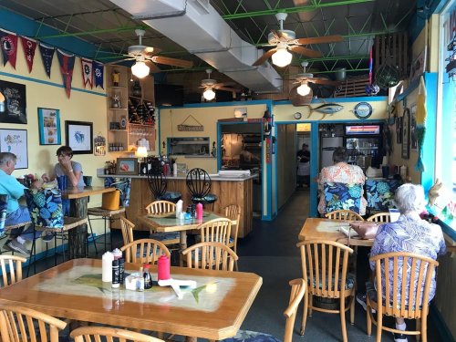 A colorful restaurant interior with wooden tables, tropical decor, and patrons enjoying their meals.