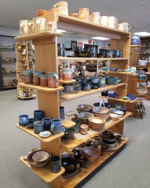 A wooden display shelf filled with various handcrafted pottery, including mugs, bowls, and pitchers in different colors.