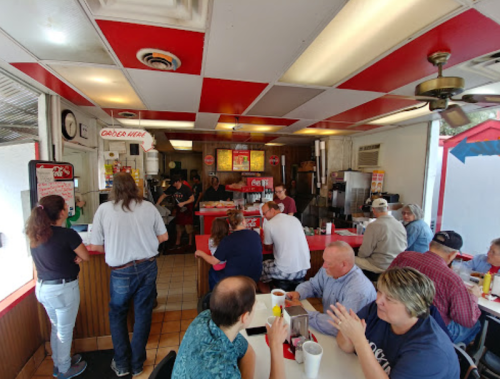 A busy diner with red and white decor, featuring customers seated and ordering at the counter.
