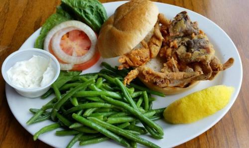 A plate featuring a fried soft-shell crab sandwich, lettuce, tomato, green beans, and a lemon wedge.