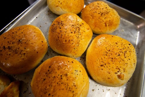 Freshly baked golden-brown rolls sprinkled with black pepper, arranged on a metal tray.