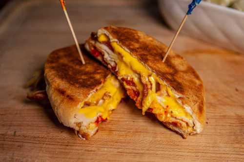 A toasted sandwich filled with melted cheese, bacon, and other ingredients, secured with two colorful toothpicks.