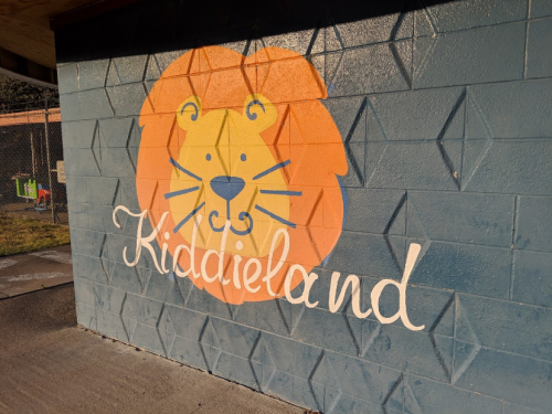 A colorful mural of a lion's face with the text "Kiddieland" beneath it on a textured wall.