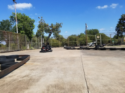 A go-kart on a track surrounded by tires, with trees and a blue sky in the background.