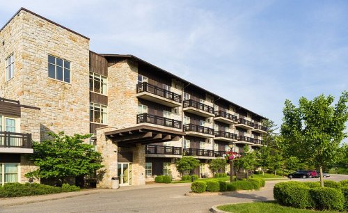 A modern stone building with balconies, surrounded by greenery and a clear blue sky.
