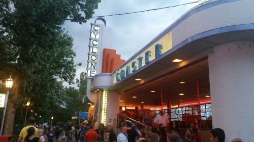 Entrance to the Cyclone roller coaster, with colorful signage and a crowd of people enjoying the amusement park.