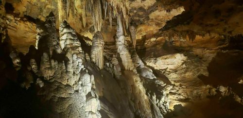 Stalactites and stalagmites in a dimly lit cave, showcasing intricate rock formations and textures.