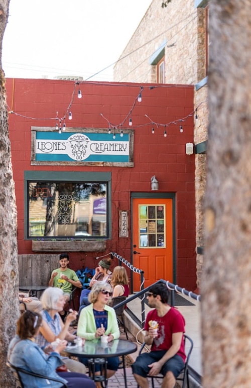 A group of people enjoying ice cream outside Leone's Creamery, with colorful decor and trees framing the scene.