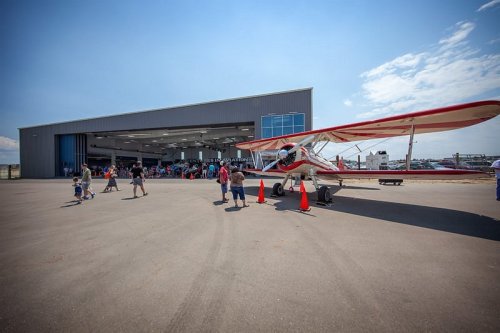 A biplane parked outside a hangar with people walking around during an aviation event.