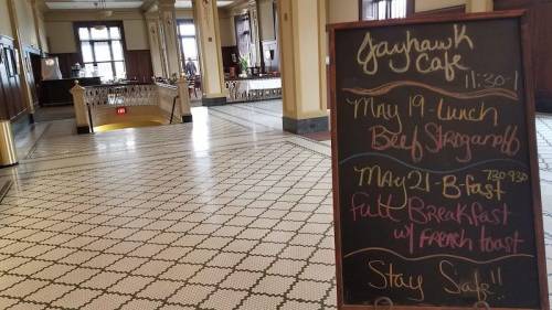 A chalkboard menu outside the Jayhawk Cafe, listing lunch and breakfast specials in a spacious, elegant interior.