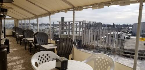 A covered outdoor seating area with chairs and tables, overlooking a wooden dock and water in the background.