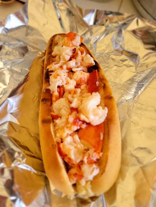 A lobster roll filled with chunks of lobster meat, served in a toasted bun on a sheet of foil.