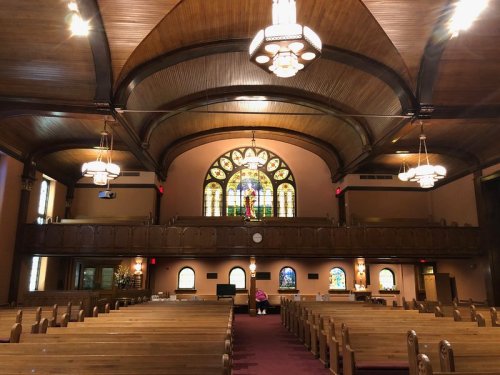 Interior of a church featuring wooden pews, a high ceiling, and a colorful stained glass window.