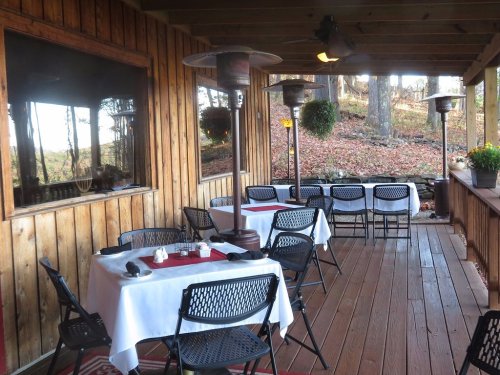 Cozy outdoor dining area with tables, chairs, and patio heaters, surrounded by trees and autumn leaves.