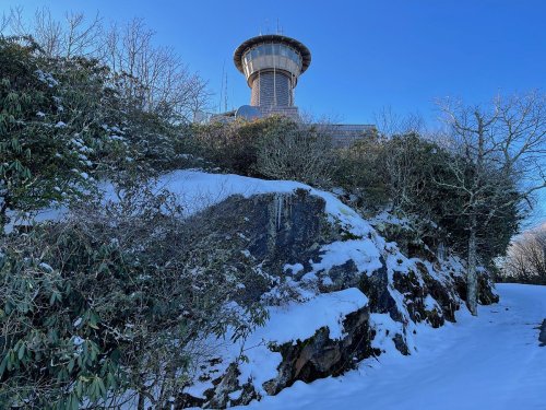 A snowy landscape with a rocky outcrop and a tall building in the background against a clear blue sky.