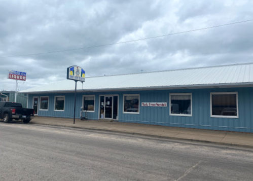 A blue storefront with a metal roof, featuring a liquor sign and a sign that reads "Talk From Scratch."