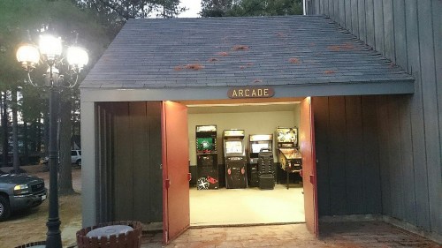 Entrance to an arcade with game machines visible inside, framed by a rustic building and outdoor lighting.