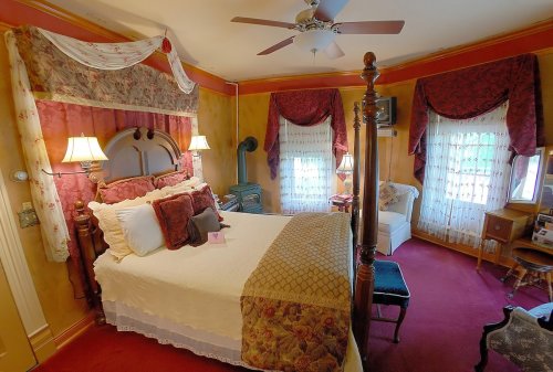 Cozy bedroom with a four-poster bed, decorative curtains, and warm colors, featuring a sitting area and soft lighting.