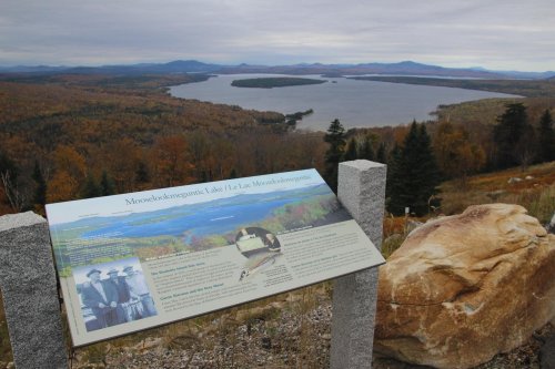 Scenic view of Moosehead Lake surrounded by autumn foliage, with an informational sign in the foreground.